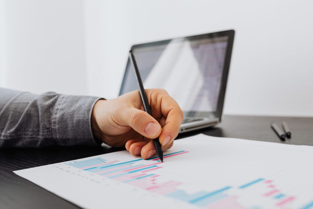 Person taking notes on a business chart with a laptop in the background.
