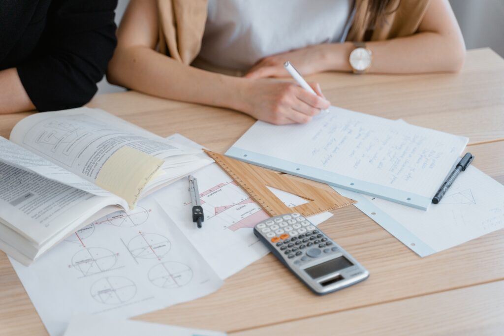 pexels photo 8472980 8472980 Person writing notes with books and calculator, ideal for study and education themes.